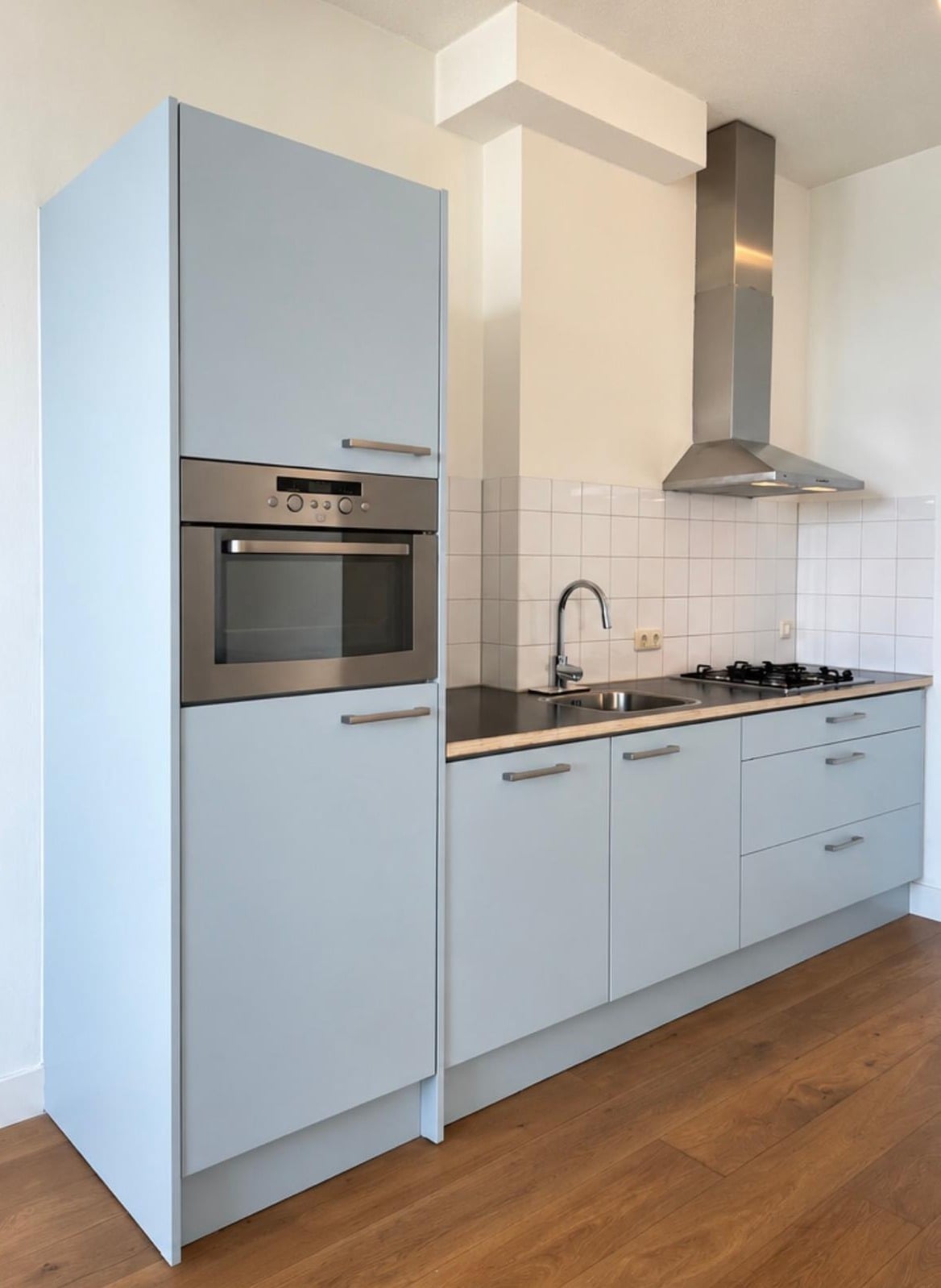 Keuken met lichtblauwe fronten, een hoge ovenkast en een rechte onderkastenwand, voor het wrappen